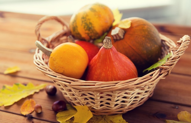 concepto de cosecha, temporada, publicidad y otoño - cierre de calabazas en una cesta de mimbre con hojas sobre una mesa de madera en casa