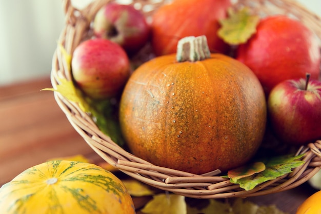 concepto de cosecha, temporada, publicidad y otoño - cierre de calabazas en una cesta de mimbre con hojas sobre una mesa de madera en casa