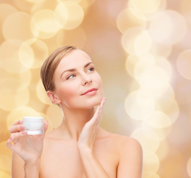 concepto de cosmética, salud y belleza - hermosa mujer aplicando crema en su piel