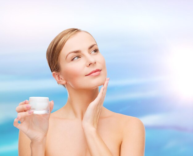 concepto de cosmética, salud y belleza - hermosa mujer aplicando crema en su piel