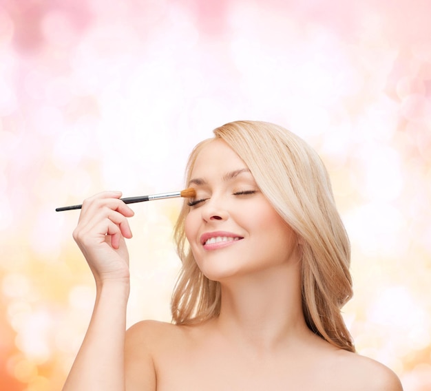 concepto de cosmética, salud y belleza - mujer hermosa con los ojos cerrados y pincel de maquillaje