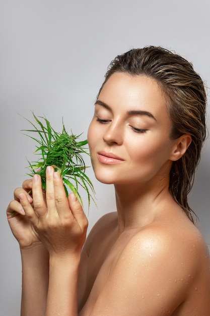 Concepto de cosméticos de CBD. Bella mujer con una hoja de cannabis sobre fondo gris