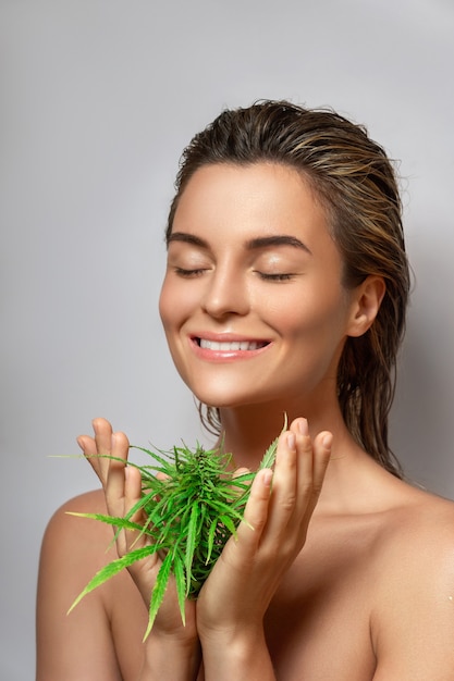 Foto concepto de cosméticos de cbd. bella mujer con una hoja de cannabis sobre fondo gris