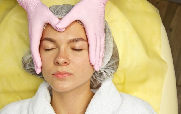 Concepto de cosmetología Cerrar las manos de esteticista limpiando y tocando una cara femenina con una esponja Una mujer está acostada y descansando