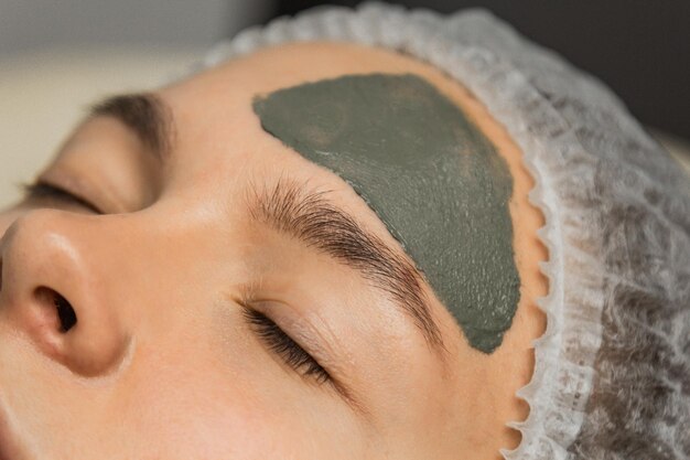 El concepto de cosmetología Primer plano de una esteticista aplicando una máscara verde con un cepillo en la cara de una mujer
