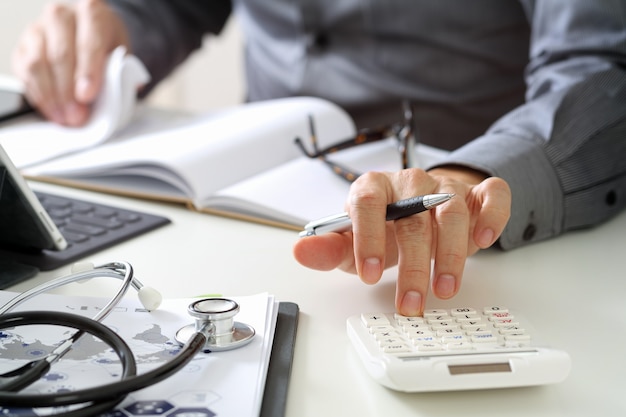 Concepto de costos y tarifas de salud. La mano del doctor elegante utilizó una calculadora para los costes médicos en hospital.