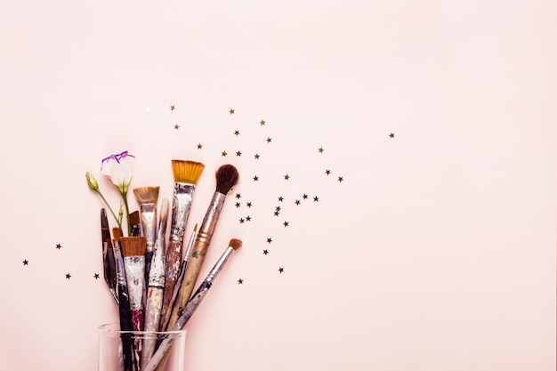 Concepto de creatividad. Art Brush Set y dispersión de estrellas doradas sobre fondo rosa pastel.