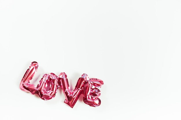 Concepto creativo del día de San Valentín. Signo inflable de palabra de globo de lámina brillante rosa Amor con sombras aisladas sobre fondo blanco. Vista superior plana con espacio de copia. Composición ligera y brillante