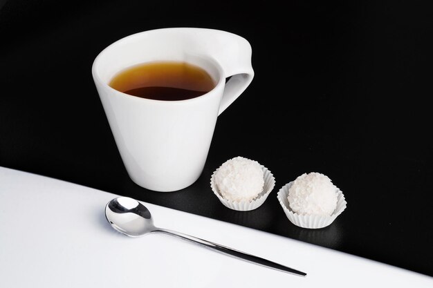 Concepto creativo de taza de té blanco con cuchara y dulces sobre fondo blanco y negro