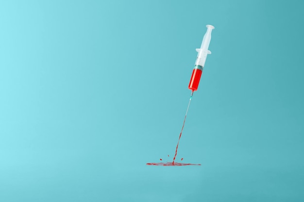 Concepto creativo de vacunación sobre un fondo azul Jeringa médica arrojando líquido rojo con salpicaduras