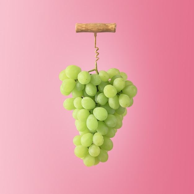 Foto el concepto creativo de la vinificación. un racimo de uvas con un sacacorchos de vino sobre un fondo rosa.