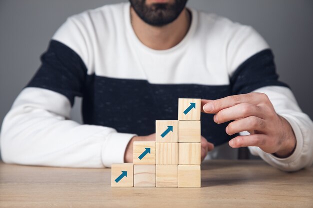 Concepto de crecimiento profesional. Hombre que sostiene los cubos de madera en la parte superior con flechas.