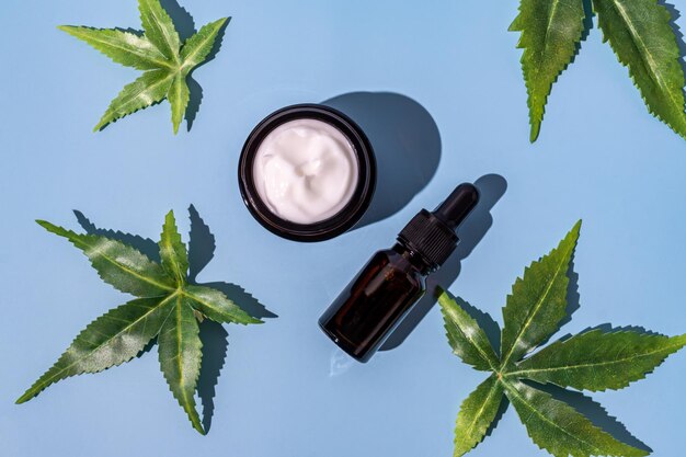 Foto el concepto de crema facial o suero o gotero de aceite de cannabis aceite cosmético natural de cbd tintura de thc y hojas de cáñamo sobre un fondo azul