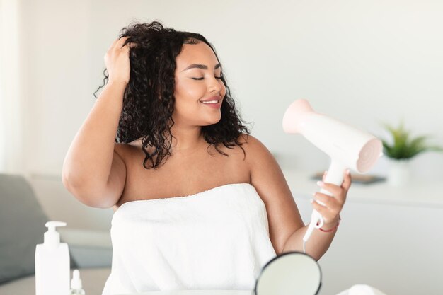 Foto concepto de cuidado del cabello femenino cuerpo afroamericano dama positiva secado y peinado del cabello con secador de pelo