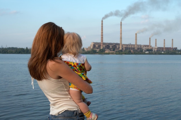 concepto de "cuidado futuro". La joven madre con sus hijos está mirando los tallos de la chimenea que contaminan el aire