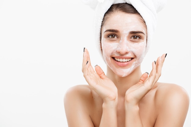 Concepto de cuidado de la piel de belleza - Retrato de rostro de mujer caucásica hermosa aplicando máscara de crema en su pared blanca de piel facial.