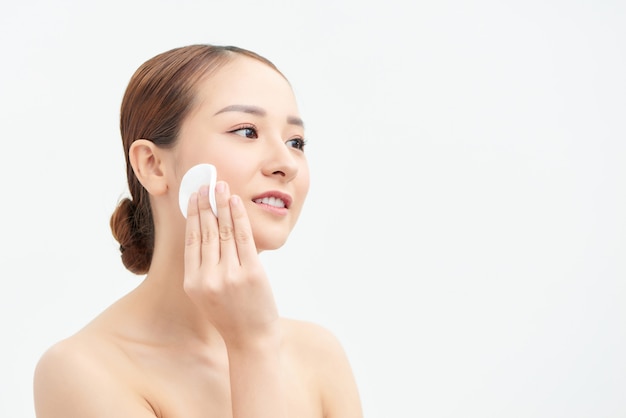 Concepto de cuidado de la piel. Hermosa mujer limpiando la piel con un algodón sobre pared blanca