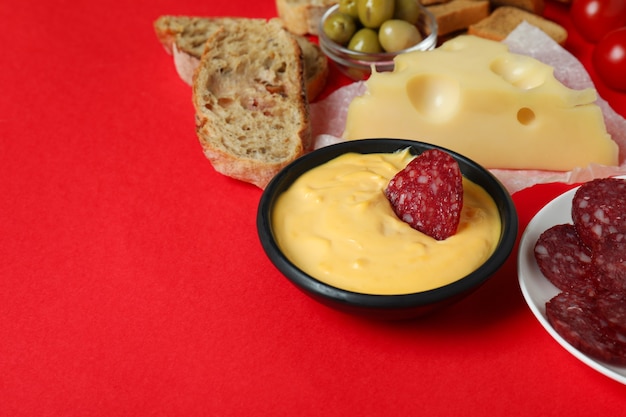 Concepto de deliciosa comida con fondue sobre fondo rojo.