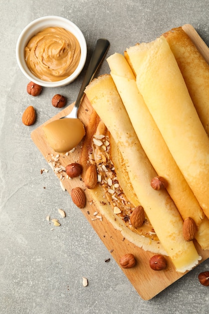 Concepto de delicioso desayuno con crepes con mantequilla de maní y nueces en mesa gris