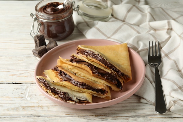 Concepto de delicioso desayuno con crepes con pasta de chocolate sobre fondo blanco de madera