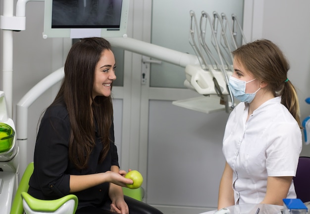 Concepto de dentista. Paciente feliz en el sillón dental con manzana verde