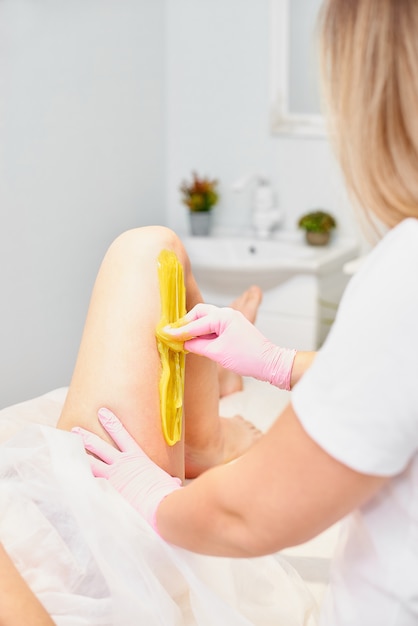 Concepto de depilación y belleza: esteticista depila las piernas de una mujer joven con azúcar líquido en el centro de spa. depilación de piernas con pasta amarilla para pegar