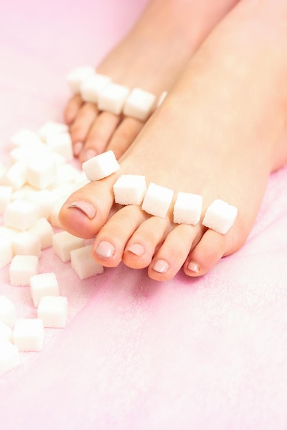 El concepto de depilación con cera Cubos de azúcar acostados en una fila sobre los dedos de los pies femeninos sobre fondo rosa