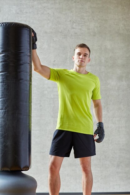 concepto de deporte, caja y gente - joven con guantes de boxeo y saco de boxeo en el gimnasio