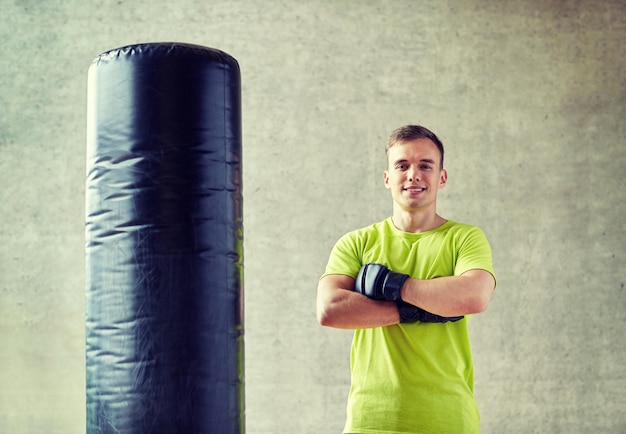 concepto de deporte, caja y gente - joven con guantes de boxeo y saco de boxeo en el gimnasio