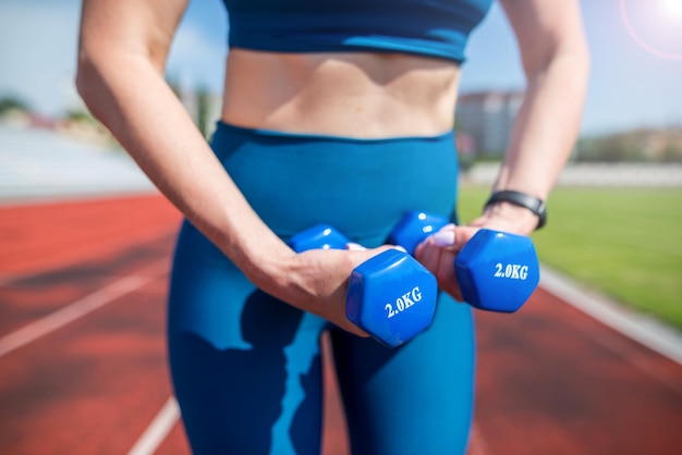 Concepto de deporte y fitness Un estilo de vida saludable Joven atleta con pesas en las manos en el estadio Una mujer hace ejercicios con pesas en un estadio deportivo