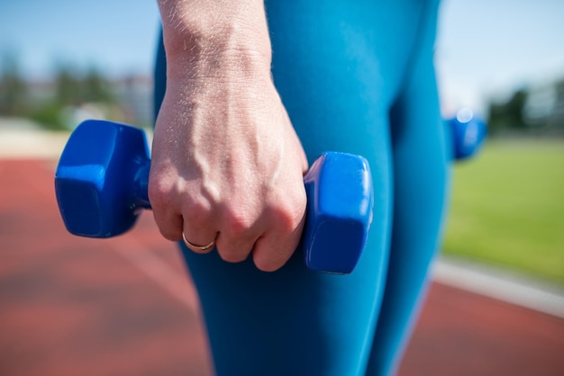 Concepto de deporte y fitness Un estilo de vida saludable Joven atleta con pesas en las manos en el estadio Una mujer hace ejercicios con pesas en un estadio deportivo