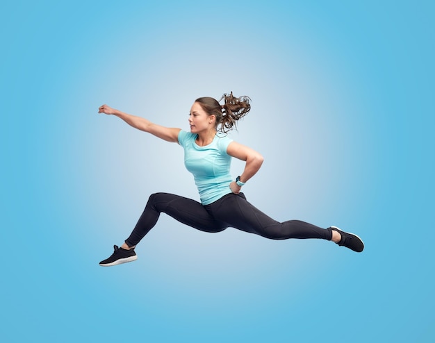 concepto de deporte, fitness, movimiento y personas - mujer joven feliz saltando en el aire en pose de lucha sobre fondo azul