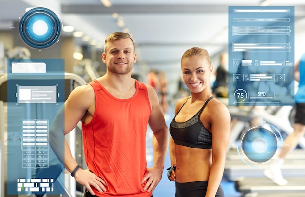 Foto concepto de deporte, fitness y personas - hombre y mujer sonrientes en el gimnasio a través de gráficos virtuales