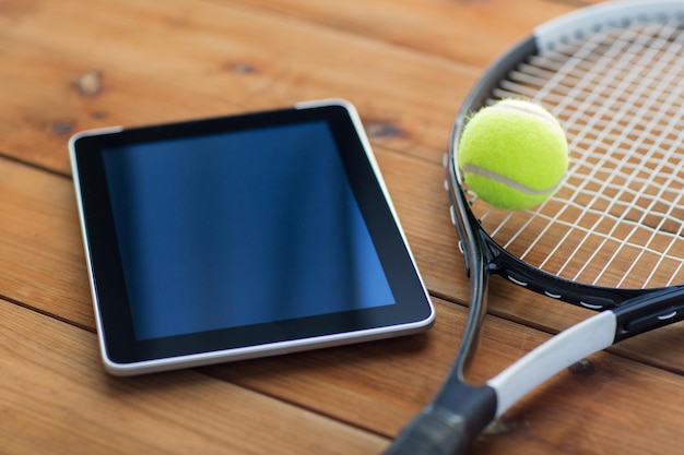 concepto de deporte, fitness, tecnología, juegos y objetos - cierre de raqueta de tenis con pelota y tablet pc en suelo de madera