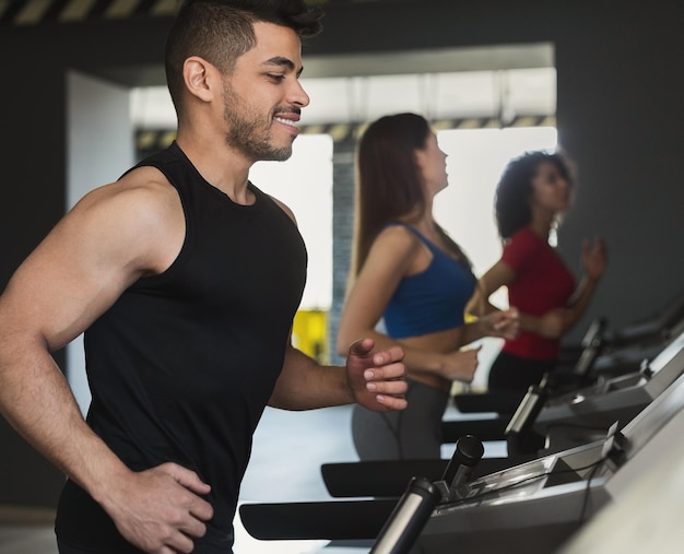 Concepto de deporte. Hombre feliz haciendo ejercicio en la caminadora en el gimnasio moderno