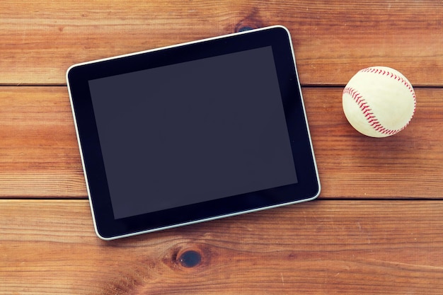 Foto concepto de deporte, tecnología, juegos y objetos: cierre de la pelota de béisbol y la computadora de la tableta en el suelo de madera