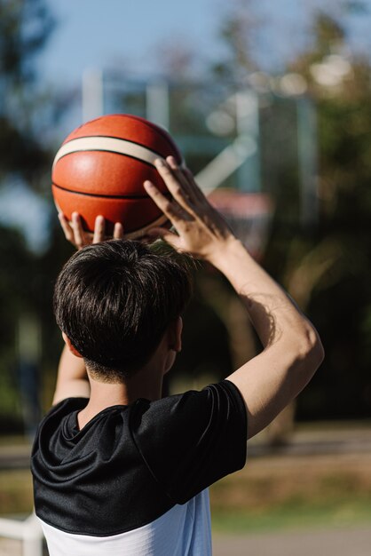 Concepto de deportes y recreación un joven adolescente practicando disparar una pelota de baloncesto por separado en la cancha después de la escuela.