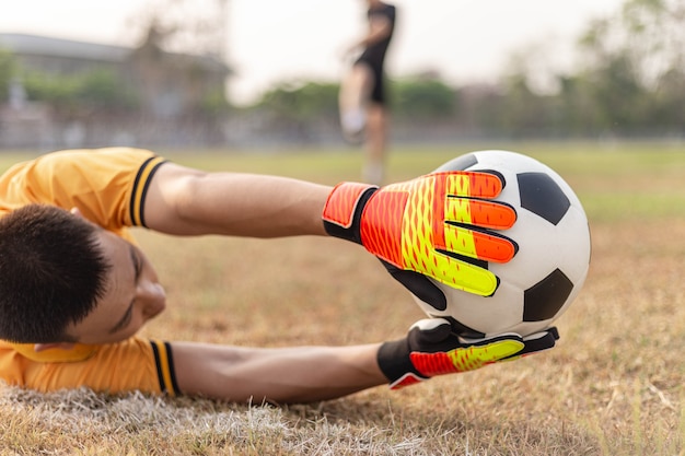 Foto concepto de deportes y recreación un joven portero masculino que usa ambas manos para atrapar el balón para evitar que el equipo contrario anote.