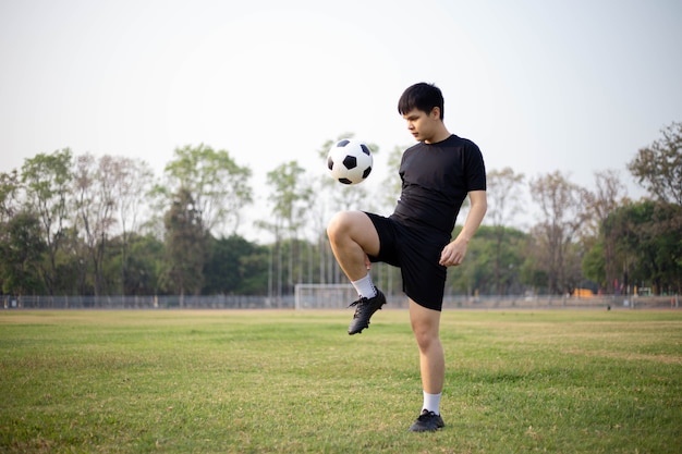 Concepto de deportes y recreación un jugador de fútbol masculino con camiseta negra y pantalones practicando patear la pelota en el campo de hierba.