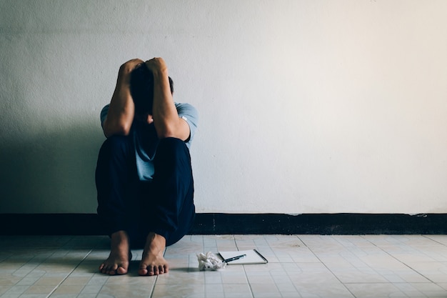 Concepto de depresión. Hombre con depresión sentado solo en el suelo en el cuarto oscuro