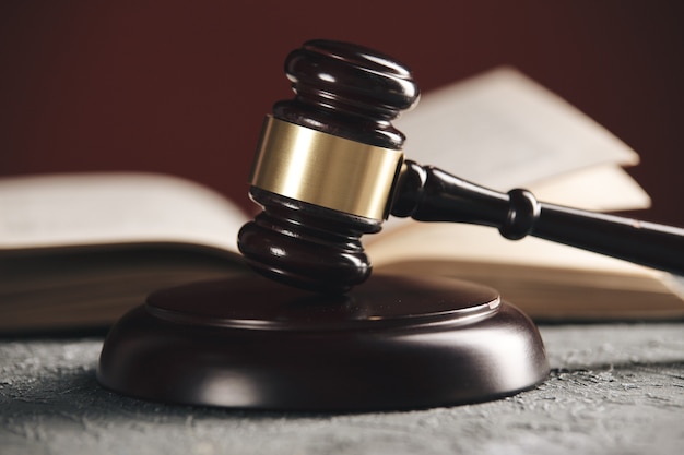 Concepto de derecho: libro de derecho abierto con un mazo de madera para jueces sobre la mesa en una sala de audiencias o una oficina de aplicación de la ley sobre fondo negro.