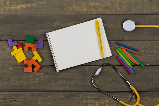 Concepto de desarrollo saludable para niños bloc de notas en blanco estetoscopio amarillo rompecabezas de madera coloridos crayones