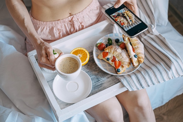 Concepto de desayuno en la cama croissant con fresas y crema en una bandeja de madera clara con una taza de café