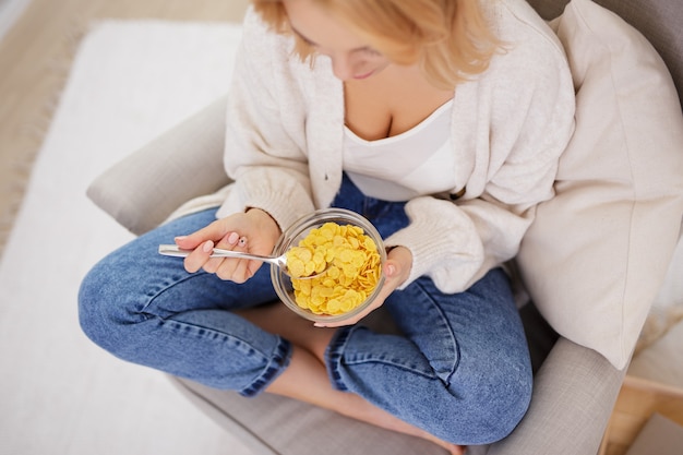 Concepto de desayuno y comida saludable - vista superior de la joven y bella mujer comiendo copos de maíz en casa