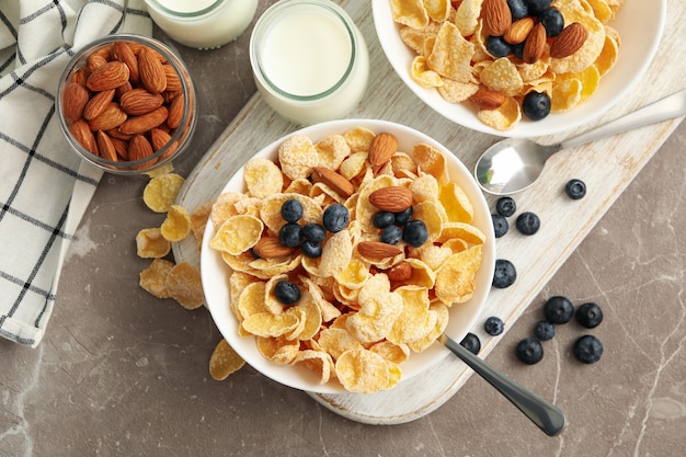 Concepto de desayuno con copos de maíz, bayas, nueces y leche en mesa gris