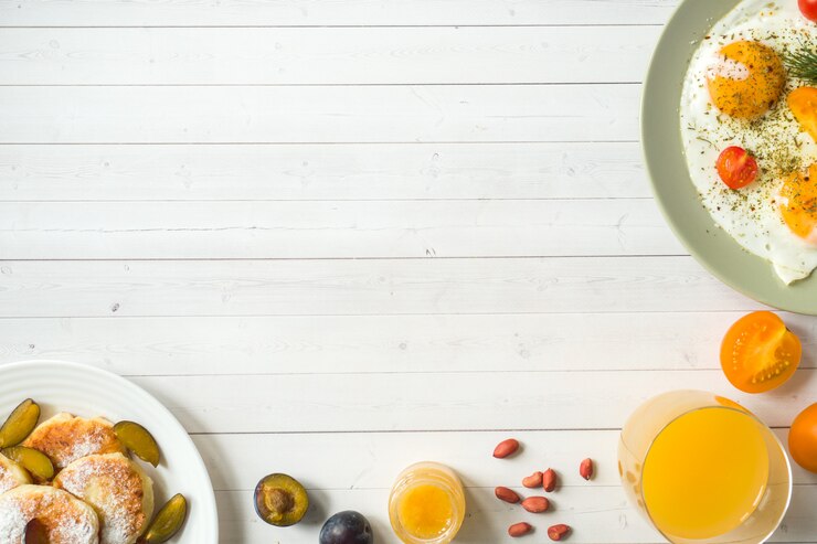 Concepto de desayuno. Huevos fritos, panqueques de requesón, ciruelas y avena con leche, jugo de naranja sobre la mesa