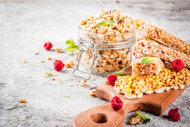 Concepto de desayuno y merienda saludable granola casera con frambuesas frescas en frasco y nueces y barras de granola sobre fondo de piedra de piedra gris