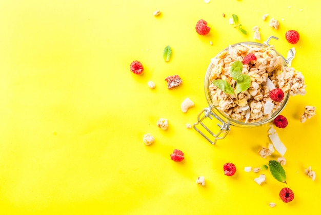 Concepto de desayuno y merienda saludable granola casera con frambuesas frescas en frasco sobre fondo amarillo brillante