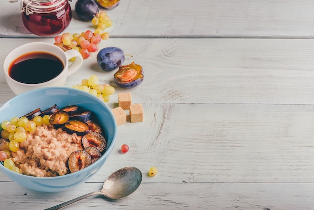 Concepto de desayuno saludable. Gachas de avena con ciruela fresca, uvas verdes y taza de café. Ingredientes sobre fondo de madera.