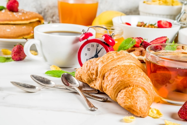 Concepto de desayuno saludable, varios alimentos de la mañana: panqueques, waffles, sándwich de avena con cruasanes y granola con yogur, fruta, bayas, café, té, jugo de naranja